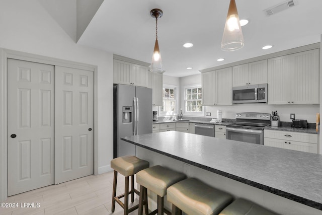 kitchen featuring white cabinetry, stainless steel appliances, a breakfast bar area, and hanging light fixtures