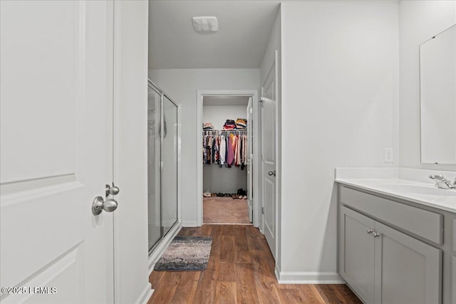 full bathroom featuring a walk in closet, baseboards, a stall shower, wood finished floors, and vanity