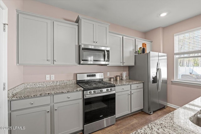 kitchen with light stone counters, appliances with stainless steel finishes, baseboards, and wood finished floors