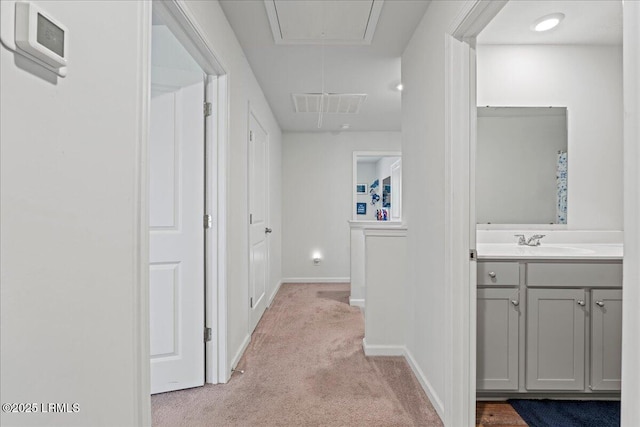 hall with visible vents, baseboards, light colored carpet, attic access, and a sink