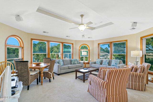 living room with light carpet, ceiling fan, a tray ceiling, and a healthy amount of sunlight