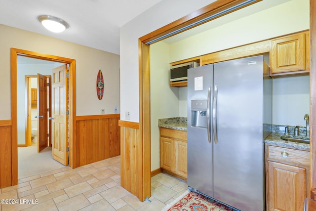 kitchen with stainless steel refrigerator with ice dispenser, wooden walls, sink, and light stone counters