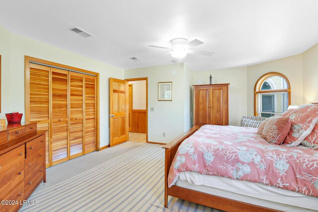 bedroom featuring light colored carpet, wood walls, ceiling fan, and a closet