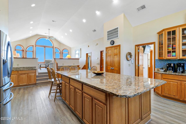 kitchen with light stone counters, vaulted ceiling, light wood-type flooring, stainless steel fridge, and a kitchen island