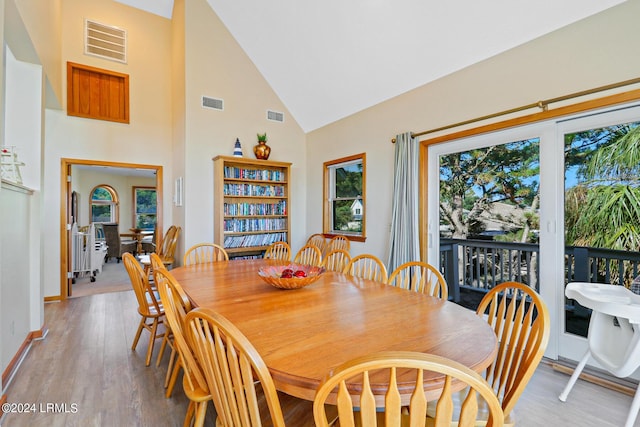 dining room with high vaulted ceiling and light hardwood / wood-style floors