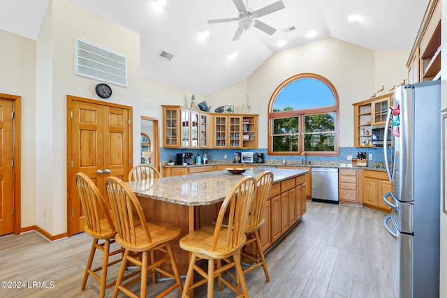 kitchen with light stone counters, a center island, light hardwood / wood-style flooring, stainless steel appliances, and decorative backsplash