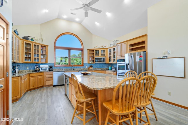 kitchen featuring a breakfast bar area, light hardwood / wood-style flooring, stainless steel appliances, a center island, and light stone counters