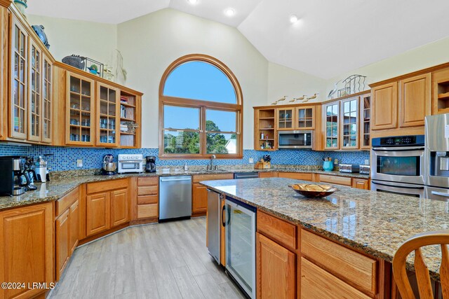 kitchen featuring sink, appliances with stainless steel finishes, wine cooler, light stone counters, and light wood-type flooring