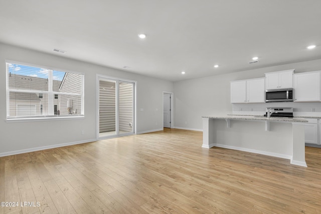 kitchen featuring a breakfast bar area, light stone counters, white cabinetry, a center island with sink, and appliances with stainless steel finishes