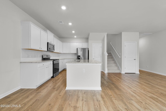 kitchen with white cabinetry, light stone counters, stainless steel appliances, and a center island with sink