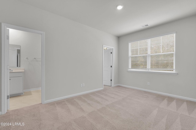 unfurnished bedroom featuring light carpet, connected bathroom, a walk in closet, and a closet