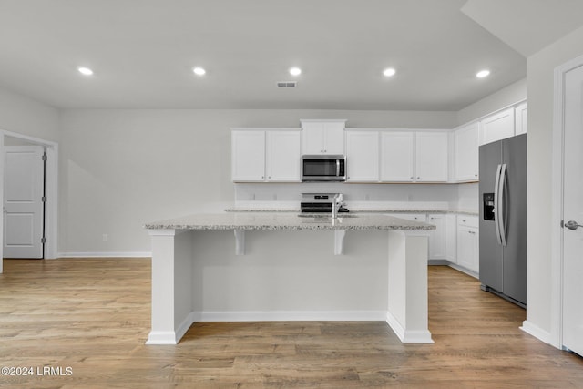 kitchen featuring appliances with stainless steel finishes, white cabinetry, light stone counters, light hardwood / wood-style floors, and an island with sink