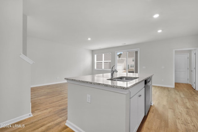 kitchen featuring sink, an island with sink, white cabinets, stainless steel dishwasher, and light wood-type flooring