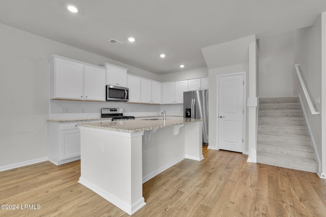 kitchen featuring stainless steel appliances, a center island with sink, white cabinets, and light stone counters