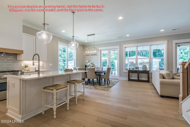 kitchen featuring stainless steel gas stove, white cabinets, a center island with sink, decorative backsplash, and light wood-type flooring