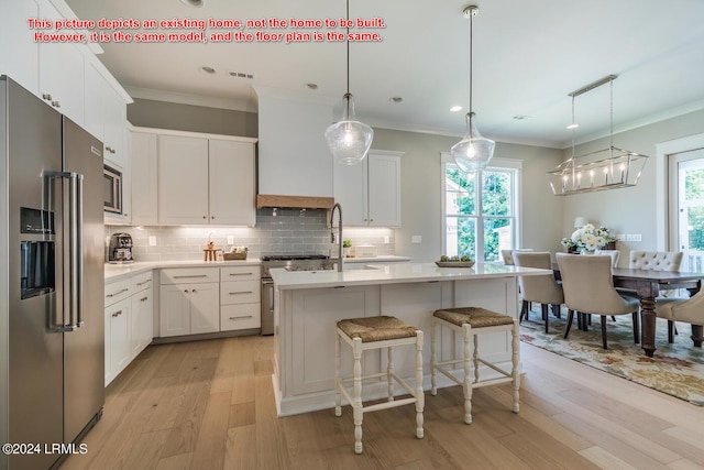 kitchen with white cabinetry, premium appliances, pendant lighting, and a kitchen island with sink