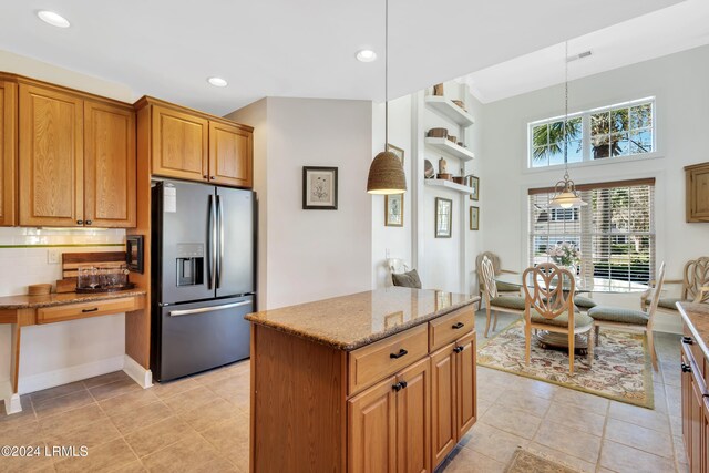 kitchen featuring stainless steel refrigerator with ice dispenser, a center island, hanging light fixtures, light stone countertops, and decorative backsplash