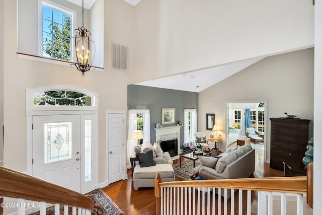 foyer entrance with wood-type flooring, high vaulted ceiling, a chandelier, and a high end fireplace