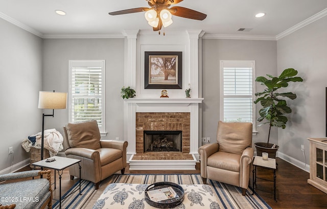 living area with crown molding, a brick fireplace, dark hardwood / wood-style floors, and ceiling fan