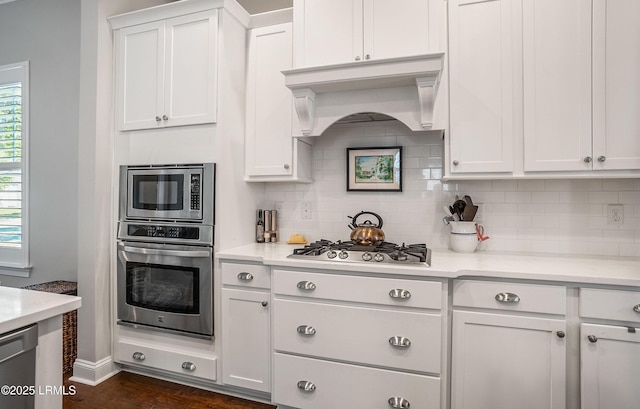 kitchen with appliances with stainless steel finishes, tasteful backsplash, white cabinetry, custom exhaust hood, and light stone counters