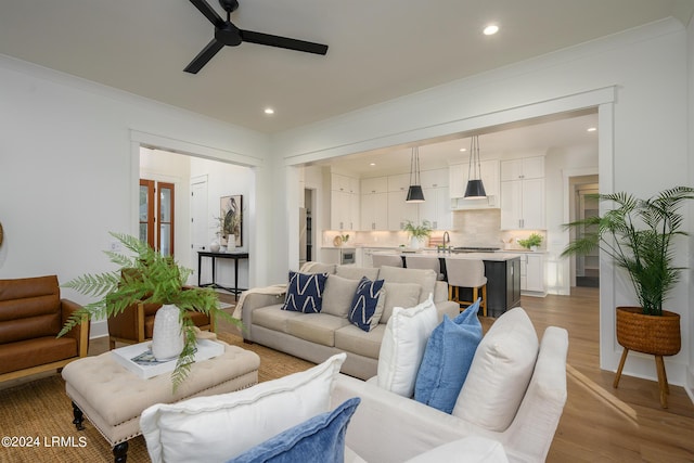 living room featuring sink, crown molding, ceiling fan, and light wood-type flooring