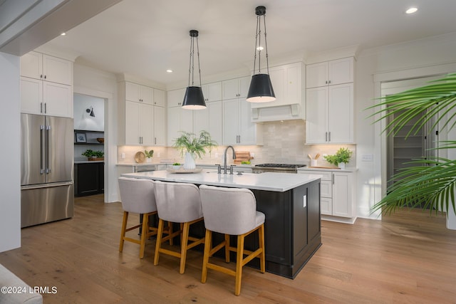 kitchen featuring high end fridge, a kitchen island with sink, and white cabinets