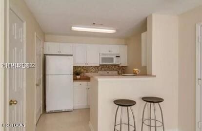 kitchen with a peninsula, white appliances, a breakfast bar, and white cabinetry