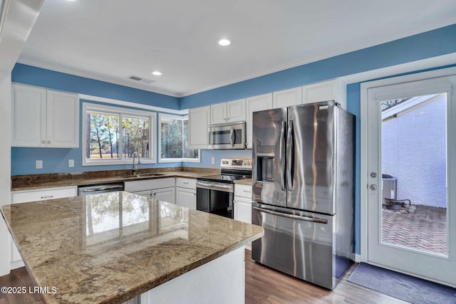 kitchen with sink, appliances with stainless steel finishes, white cabinets, a kitchen island, and light wood-type flooring