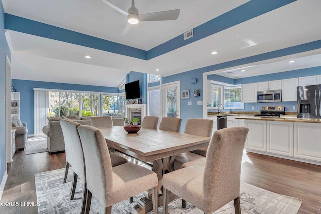 dining room with a raised ceiling, sink, ceiling fan, and light hardwood / wood-style flooring