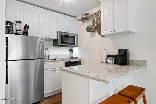 kitchen featuring a kitchen breakfast bar, kitchen peninsula, white cabinets, and appliances with stainless steel finishes