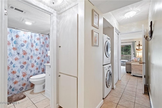 bathroom with stacked washer / drying machine, toilet, tile patterned flooring, and a textured ceiling