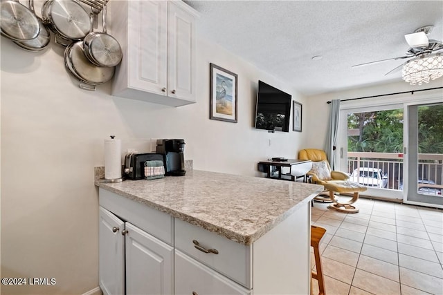 kitchen featuring light tile patterned floors, a breakfast bar area, ceiling fan, white cabinetry, and a textured ceiling