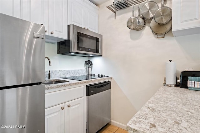 kitchen with sink, light tile patterned floors, stainless steel appliances, light stone countertops, and white cabinets