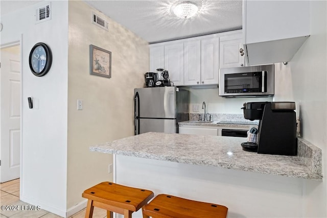 kitchen featuring a breakfast bar, sink, white cabinetry, light tile patterned floors, and appliances with stainless steel finishes