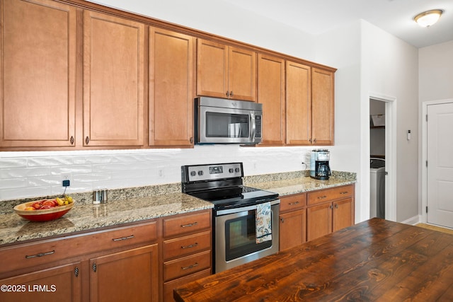 kitchen featuring appliances with stainless steel finishes, brown cabinetry, butcher block countertops, and washer / dryer