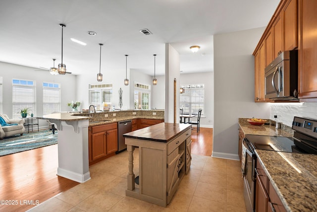 kitchen featuring pendant lighting, brown cabinets, a center island with sink, dark countertops, and appliances with stainless steel finishes