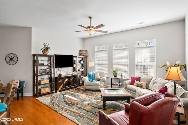 living area featuring visible vents, wood finished floors, a ceiling fan, and baseboards