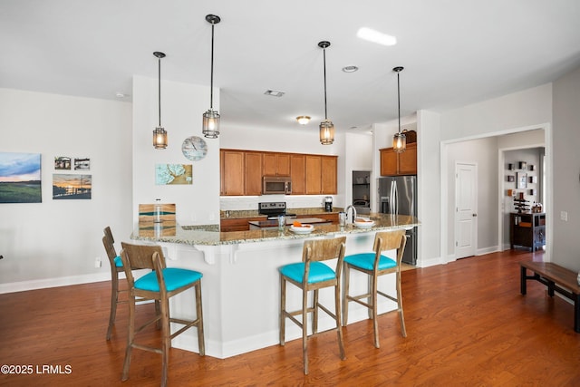 kitchen featuring dark wood-style floors, pendant lighting, brown cabinets, a breakfast bar area, and stainless steel appliances