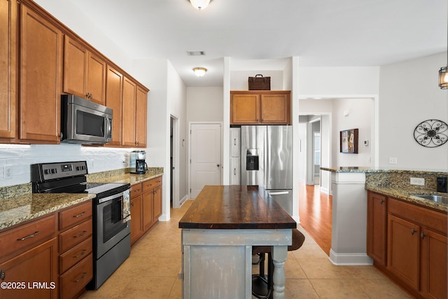 kitchen featuring dark stone counters, appliances with stainless steel finishes, brown cabinetry, and visible vents