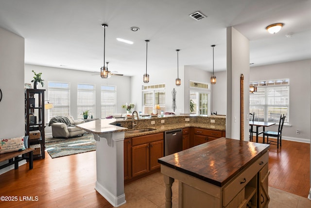 kitchen featuring brown cabinets, open floor plan, a sink, a kitchen island with sink, and stainless steel dishwasher