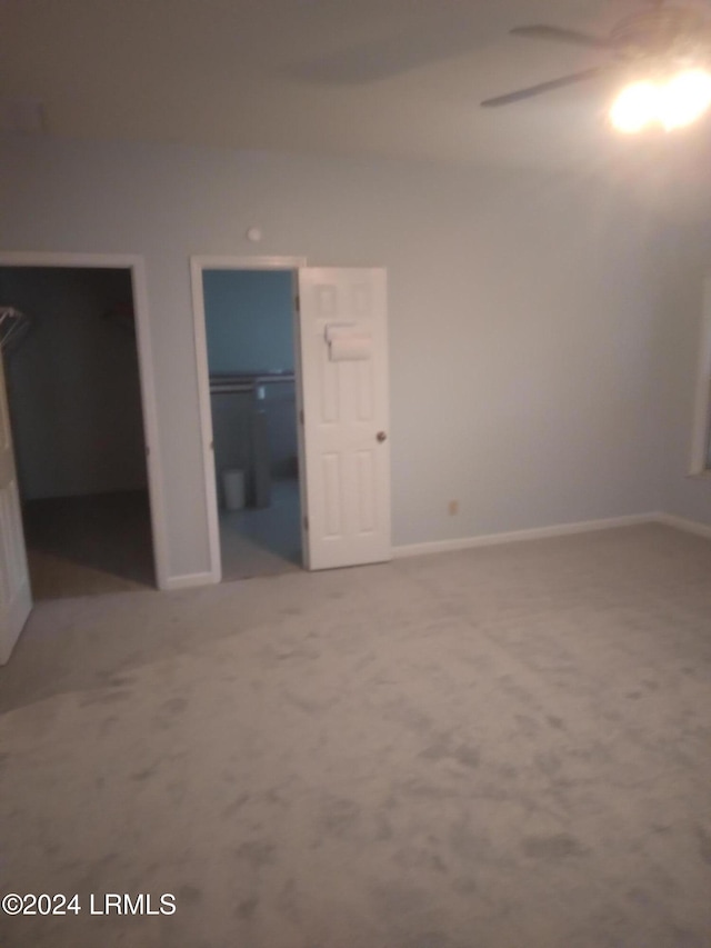 unfurnished bedroom with light carpet, a spacious closet, a closet, and baseboards