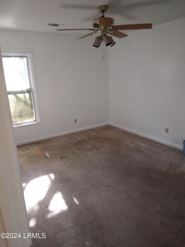 empty room featuring a ceiling fan, carpet, visible vents, and baseboards