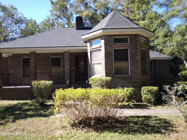 view of front facade with roof with shingles, brick siding, a chimney, and a porch