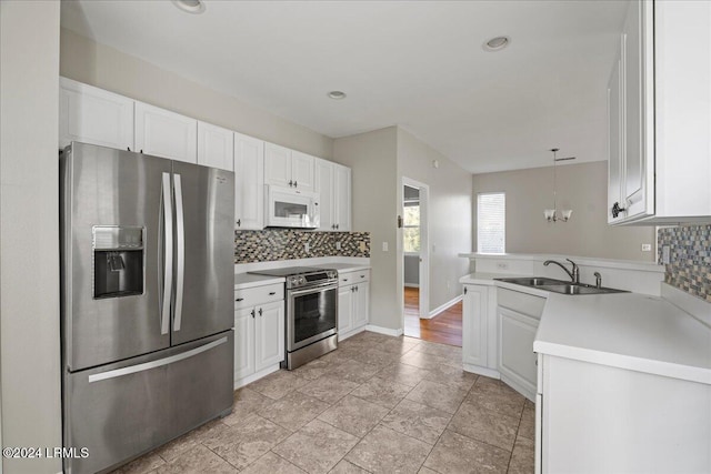 kitchen featuring appliances with stainless steel finishes, tasteful backsplash, white cabinetry, hanging light fixtures, and kitchen peninsula