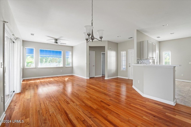 unfurnished living room featuring ceiling fan with notable chandelier and light wood-type flooring