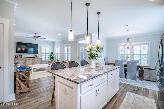 kitchen featuring decorative light fixtures, white cabinetry, a kitchen bar, a center island, and light stone counters