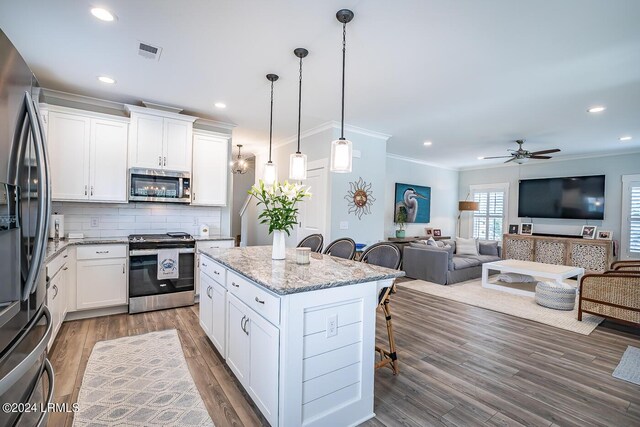 kitchen with appliances with stainless steel finishes, light stone countertops, white cabinets, a kitchen bar, and decorative light fixtures