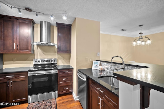 kitchen featuring wall chimney range hood, a textured ceiling, rail lighting, stainless steel appliances, and visible vents