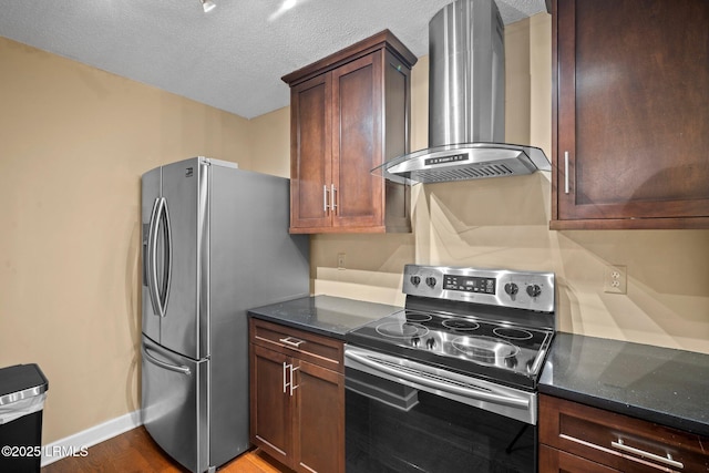 kitchen featuring a textured ceiling, baseboards, dark stone countertops, stainless steel appliances, and wall chimney exhaust hood