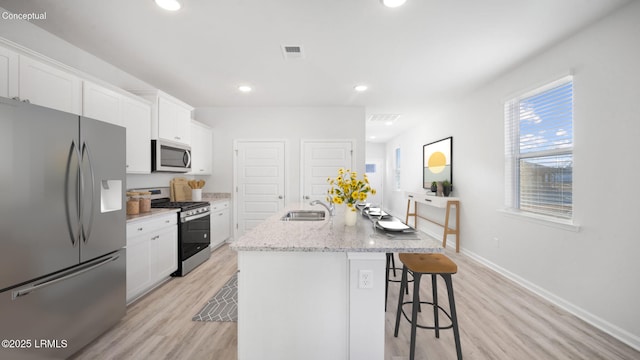 1449 Sanctum St, Ridgeland, SC 29936 - kitchen with appliances with stainless steel finishes, light wood finished floors, white cabinets, a kitchen breakfast bar, and a kitchen island with sink